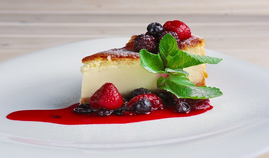 part de cheese-cake au citron et son coulis de fruits rouges sur assiette blanche